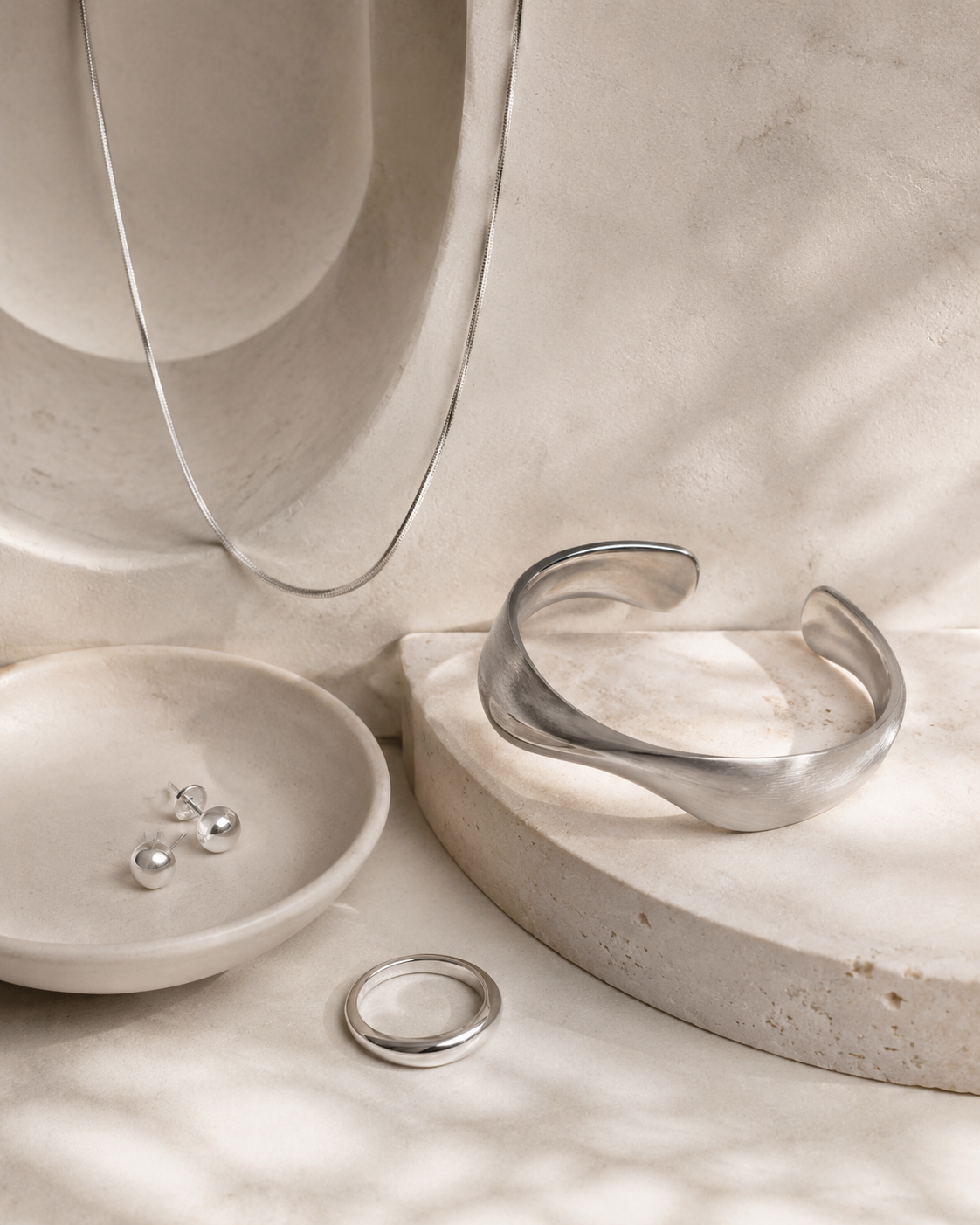Unbranded silver jewelry arranged in a warm ivory studio